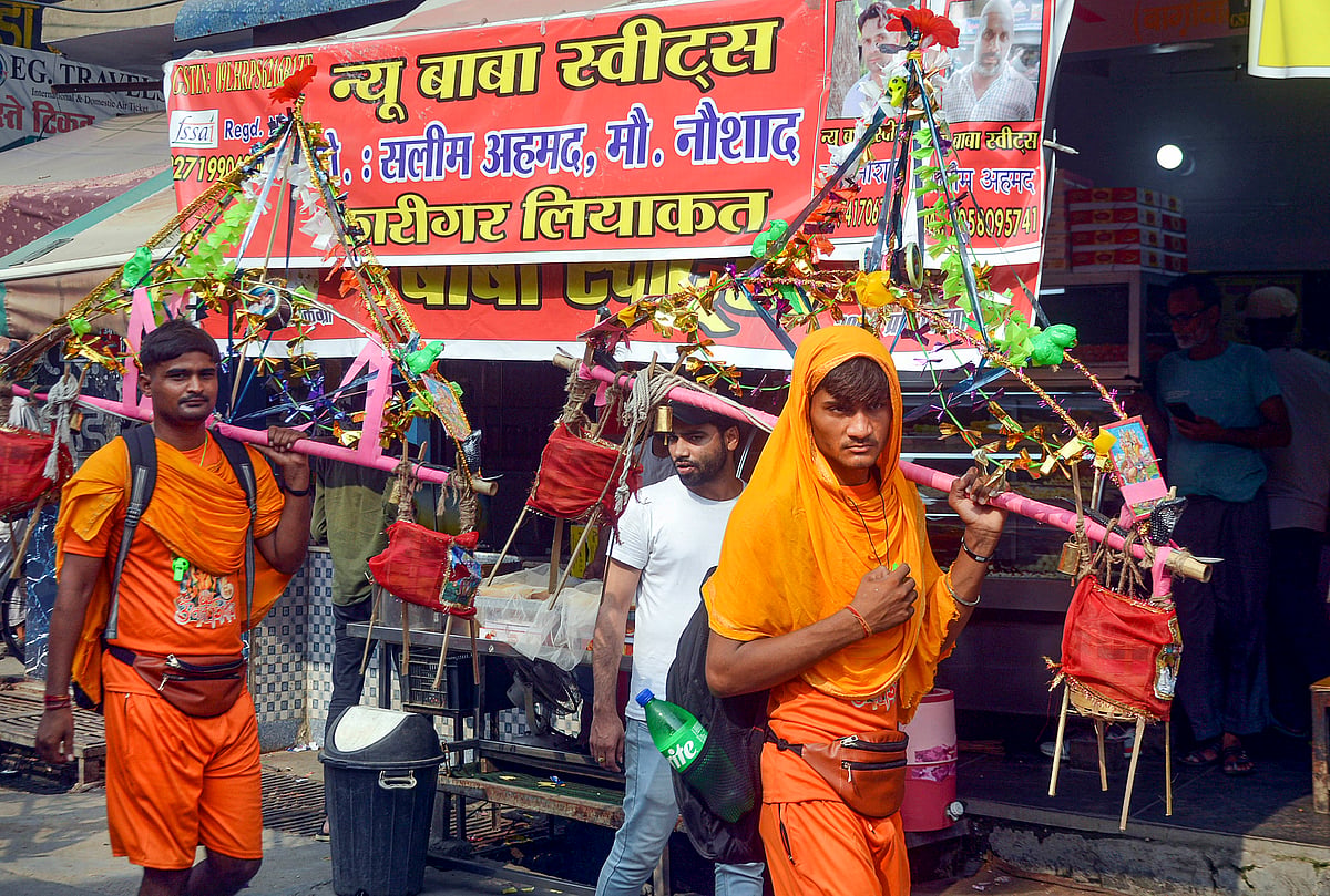 PTI : Kanwariyas walk past a shop on which banners with shopkeeper's name was put up on Kanwar Marg after an order issued by Uttar Pradesh Government, in Muzaffarnagar, Saturday, July 20, 2024. 